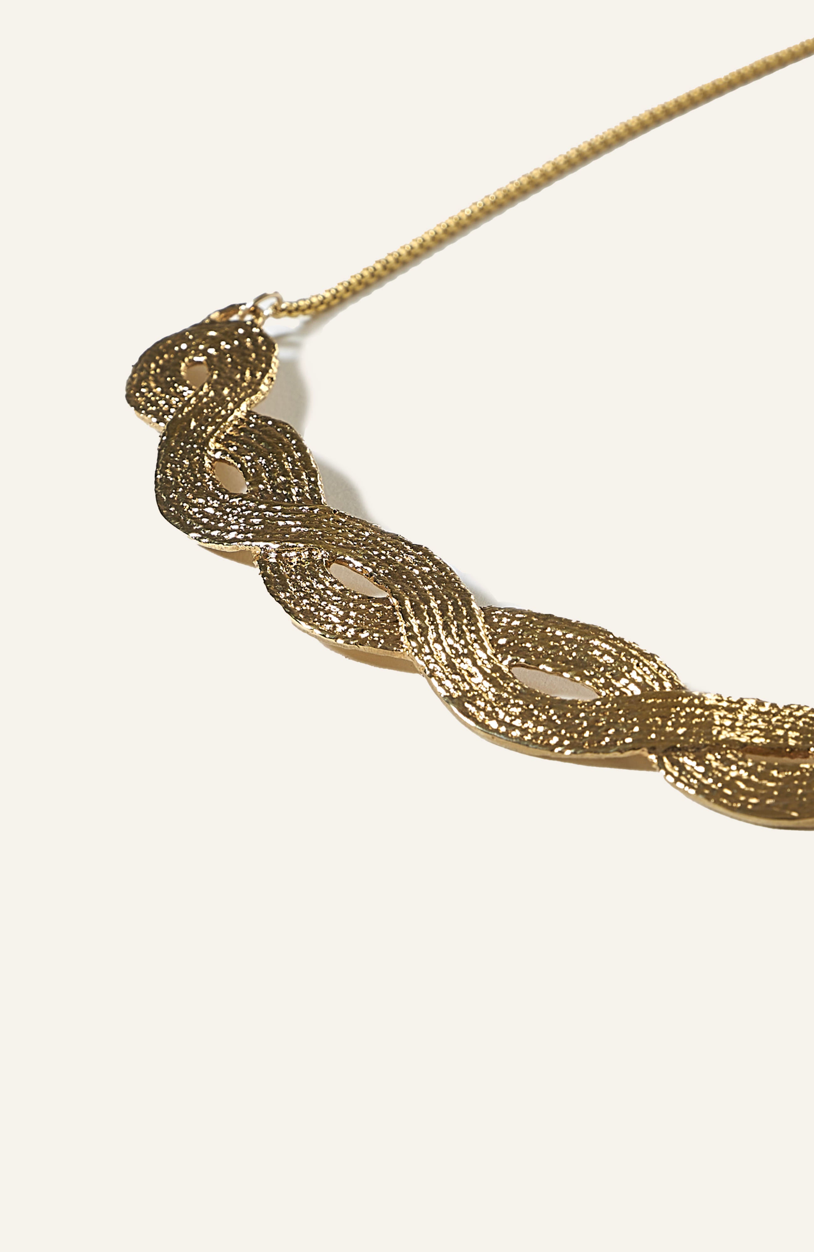 A gold-plated braid pendant necklace with an undulating, threadlike texture, displayed against a white background.