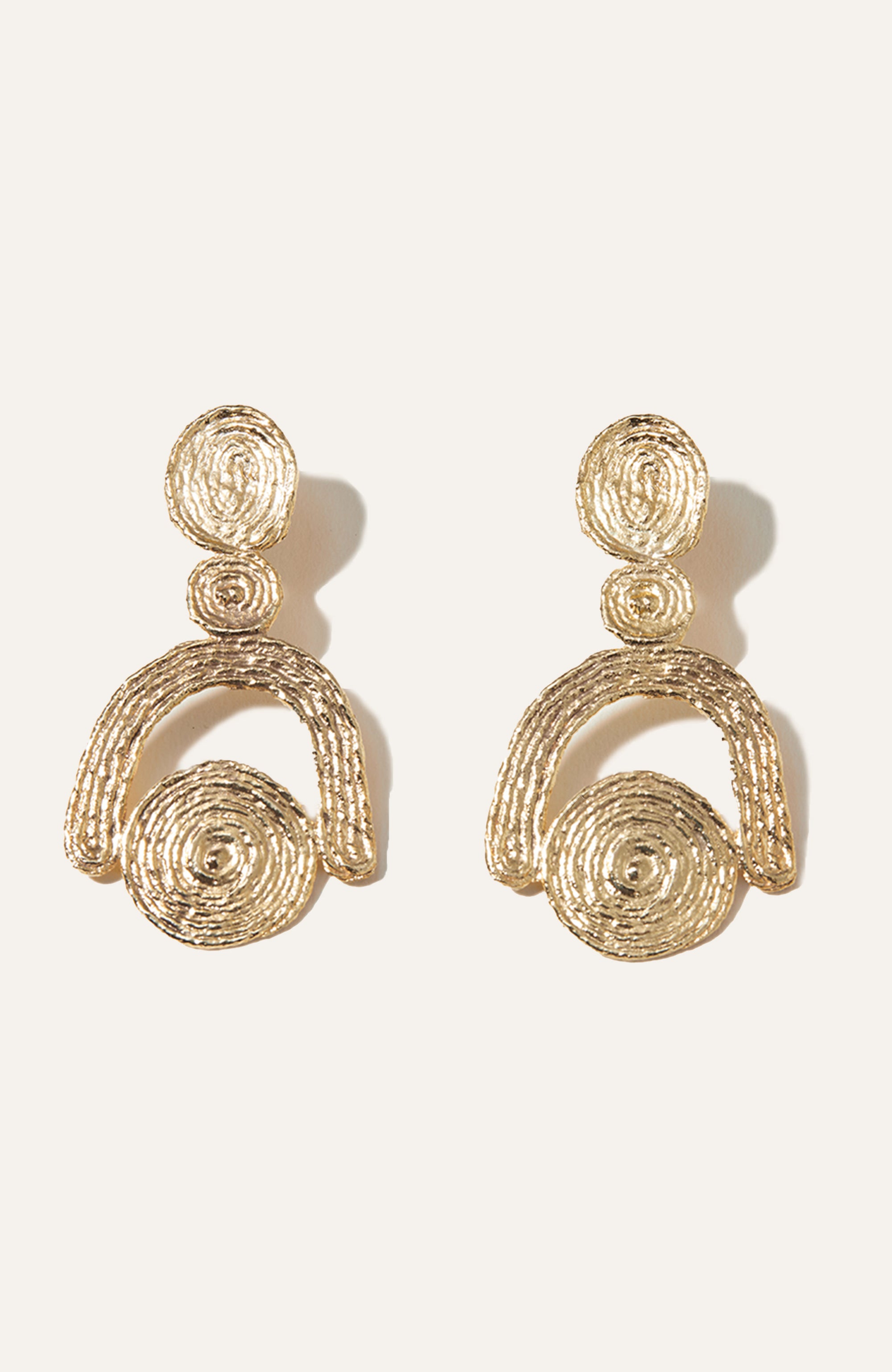A pair of gold-plated earrings with a geometric design, featuring concentric circles and woven-like curves.