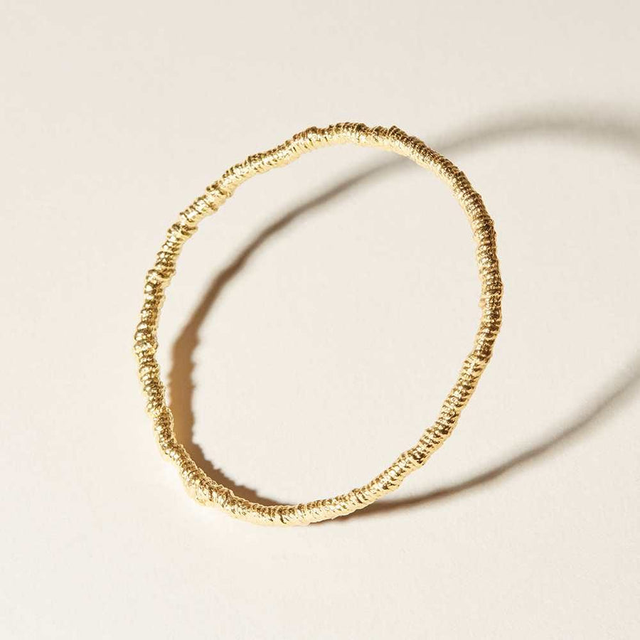 This is a bracelet that suspends threads using a casting method and is rendered in faceted, plated 14K gold plated reclaimed brass