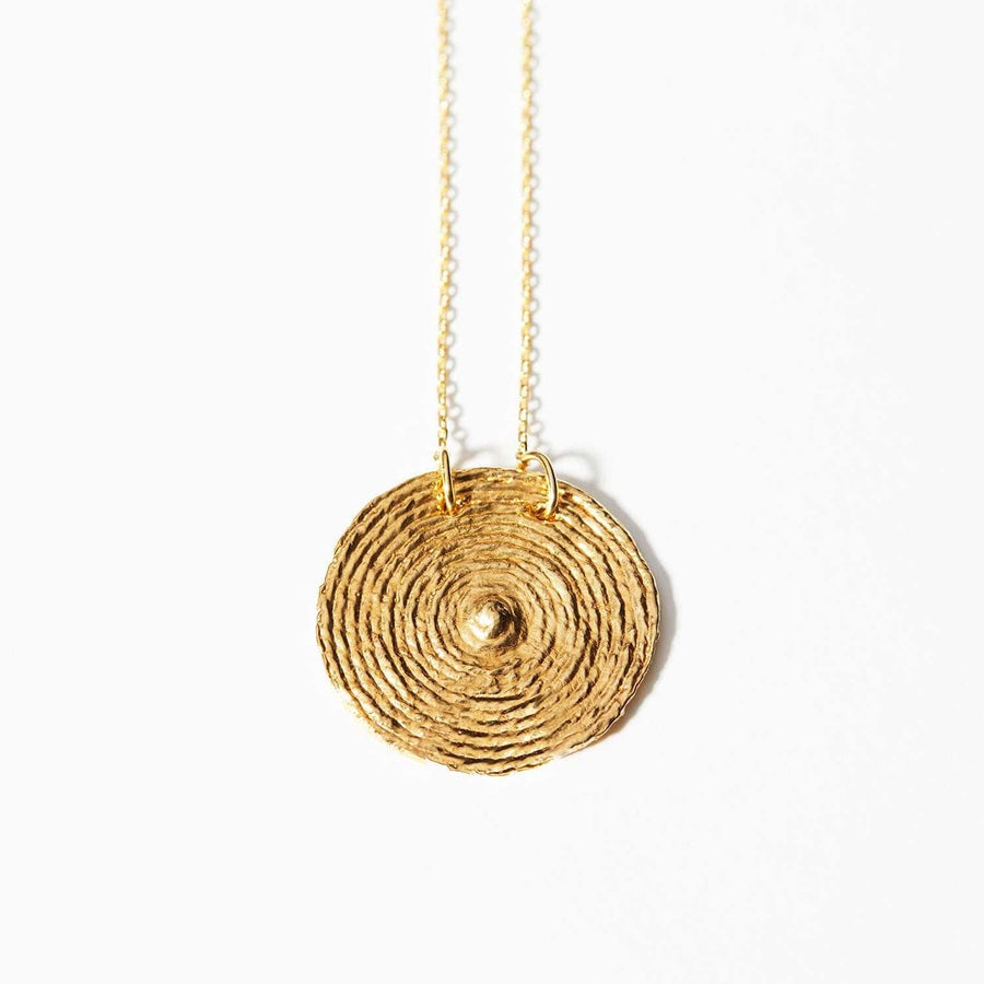 This is a 2in circular pendant that is made of patterned lines that radiate from the center. The Sol Necklace was formed by hand with cotton thread and retains its texture and dimension after being cast in 14k gold plated, reclaimed brass. 