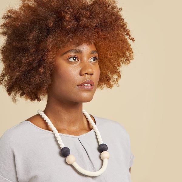 A model wears the statement necklace made of a twisted organic cord that meets stacked wooden beads and compressed felted wool. Soft and casual, this was inspired by Sailing adventures.
